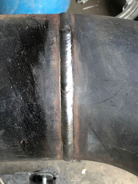 Bright welded cap bead across a dark carbon steel pipe elbow