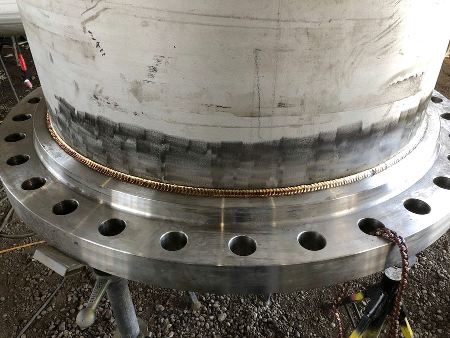 Large stainless steel column welded to a bolted flange ring, with a gold root pass around the full circumference