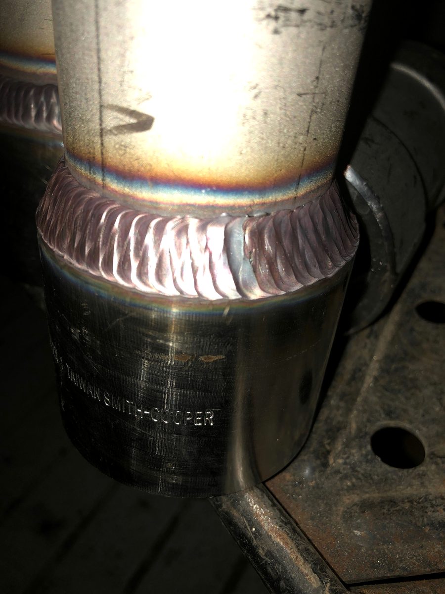 Fresh stainless pipe joint with rainbow heat tint, photographed in a dark shop